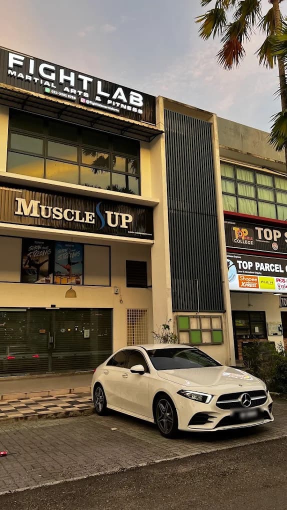 The Fightlab Martial Arts & Fitness sign on the first floor of a shop lot, above the Muscle Up sign, at dusk.