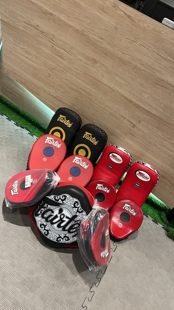 Fairtex and Twins Muay Thai pads, kick shields and focus mitts lined up against a wall at the gym.