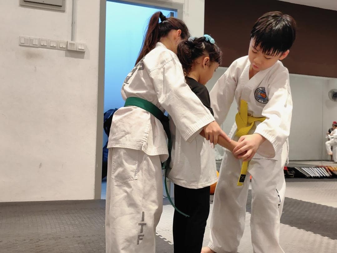 Two Taekwon-Do students help a young beginner with her arm position during class.