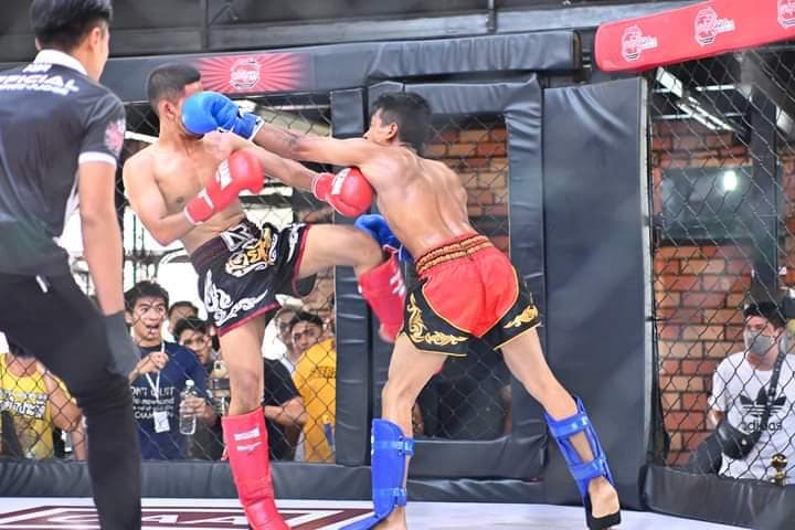 Two Muay Thai fighters exchange punches in a cage bout as the referee watches.
