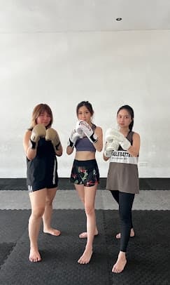Three women in boxing gloves hold their guard on the mats during a semi-private class.