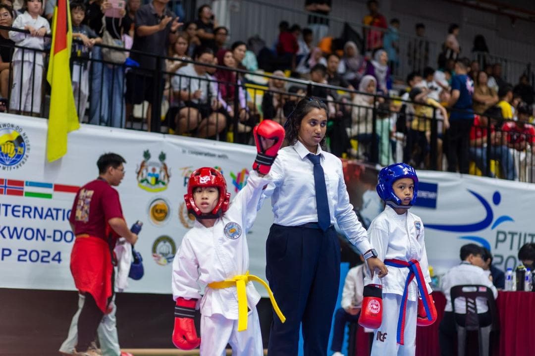 A referee raises the hand of a young Taekwon-Do student in red headgear after a sparring bout at an international championship in 2024.